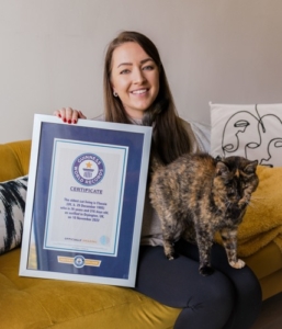 mulher morena com um gato no colo e segurando um certificado emoldurado do Guiness World Records