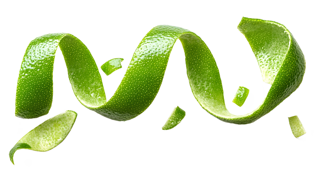 Imagem de uma longa casca de lima verde brilhante em formato espiral, destacada sobre um fundo branco. A textura da casca é visível, mostrando os poros naturais da fruta, enquanto pequenos pedaços adicionais de casca estão soltos ao redor, criando uma composição elegante e limpa.